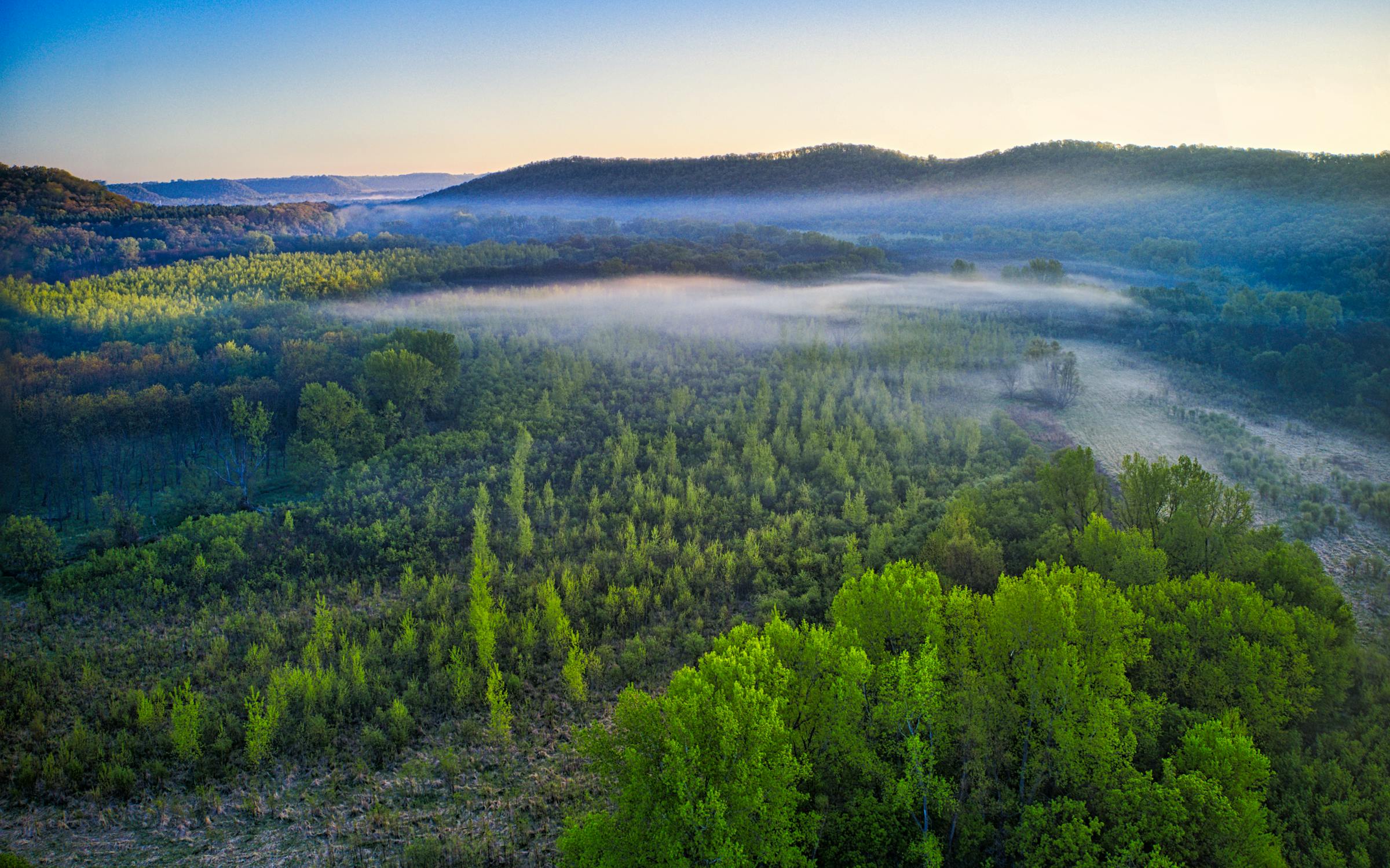 Aerial view of a misty forested river valley at sunrise across the region Apex Energy Resources serves